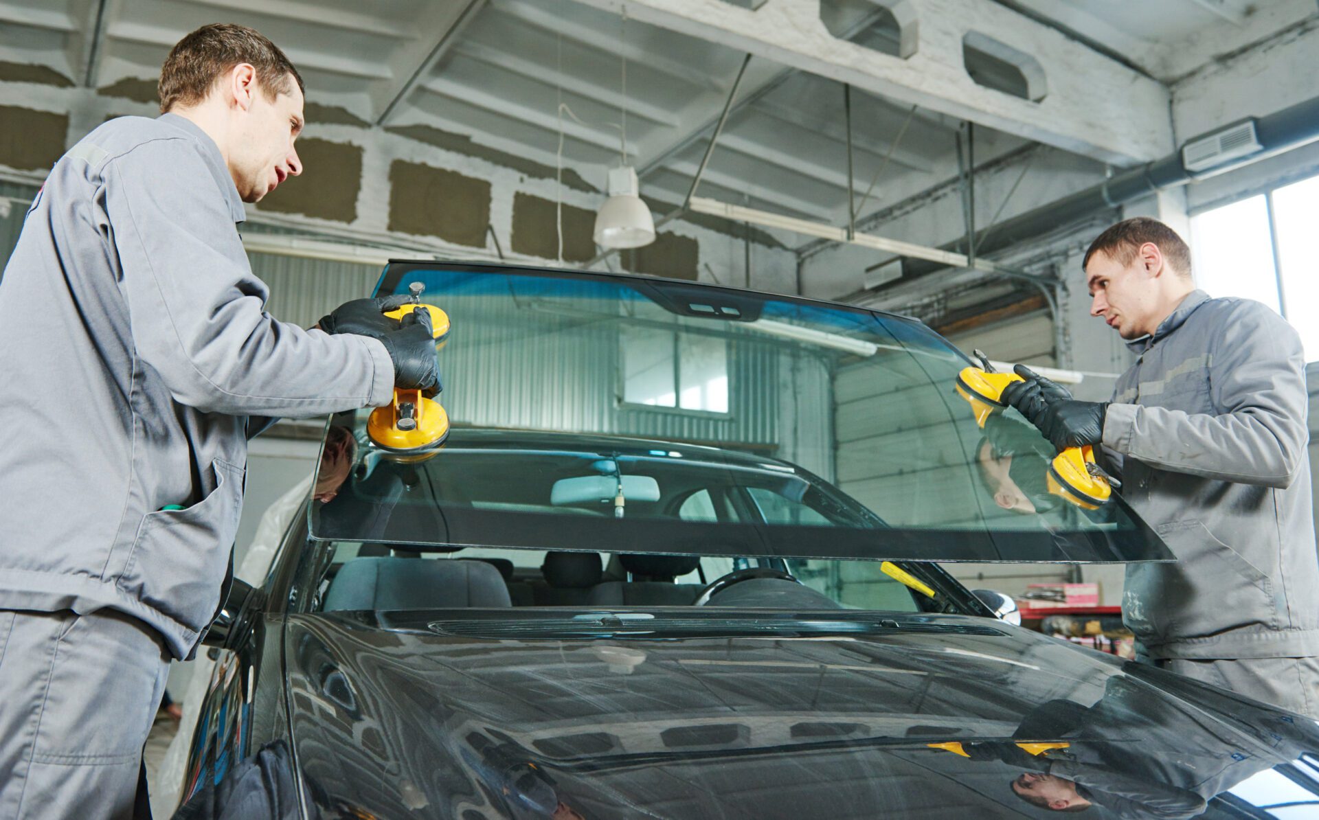 automobile windshield or windscreen replacement Glazier repairman mechanic worker replaces windshield or windscreen on a car in automobile workshop garage